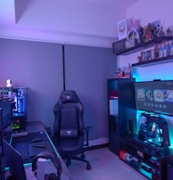 A modern gaming setup featuring a sleek gaming chair, dual monitors on a desk, and LED lighting. A gaming console and various decorations are displayed on shelves, creating an organized and vibrant gaming environment.