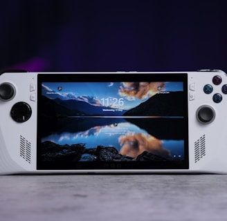 A handheld gaming console with a central screen displaying a scenic wallpaper of mountains and a lake, flanked by controller buttons and joysticks on both sides. The lighting around is dim, with purplish hues in the background, creating a modern and elegant atmosphere.